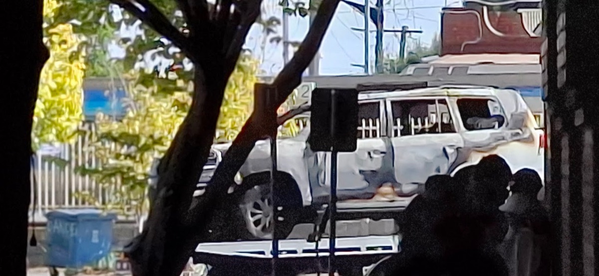 Burnt-out four-wheel drive on a suburban street, seen through trees
